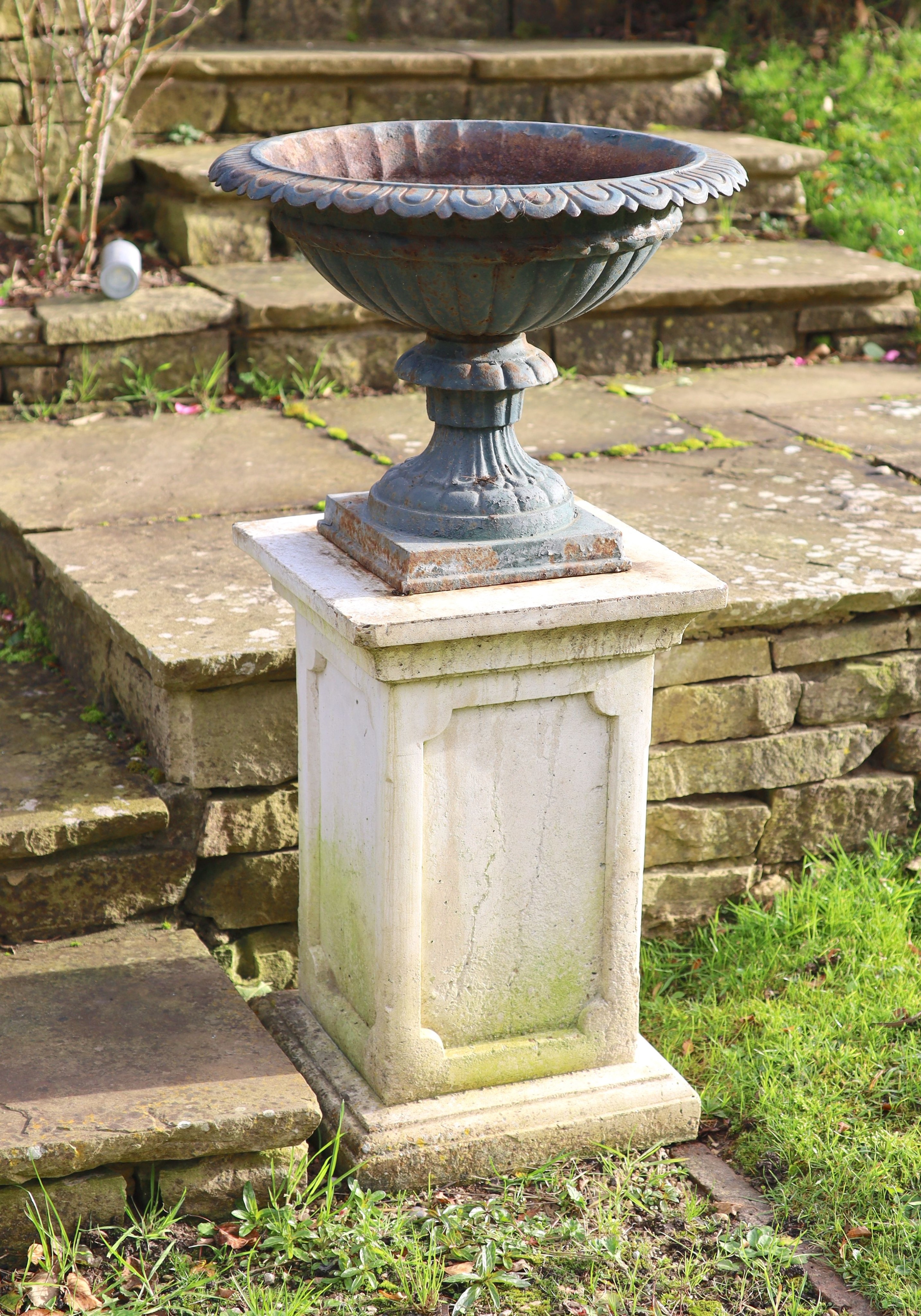 A pair of green painted cast iron garden urns on reconstituted stone pedestals, diameter 52cm height 99cm